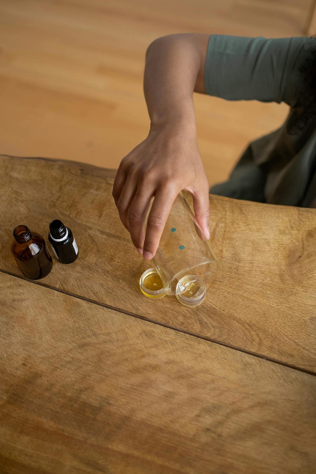 A person making natural lip balm with essential oils on a wooden table.